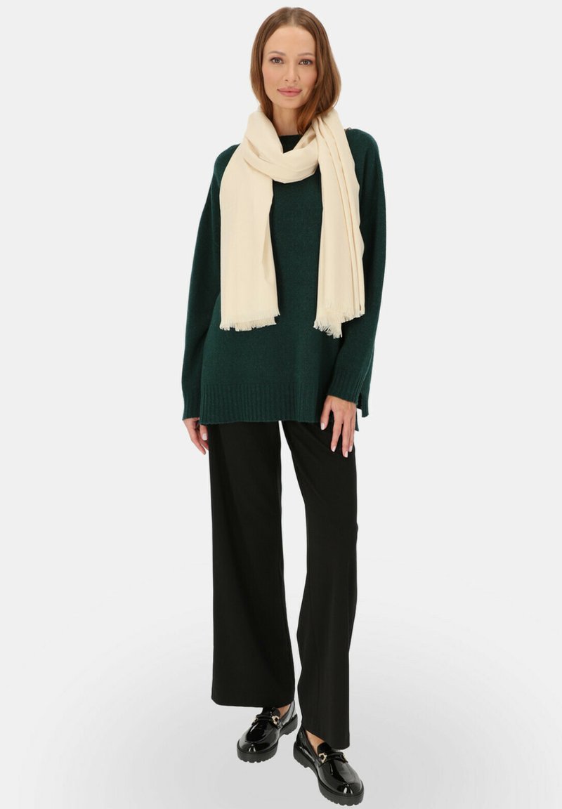 Zielony sweter robiony na drutach z ryżowym wykończeniem, zestawiony z czarnymi szerokimi spodniami. Przykrycie z kremowego szalika dodaje kontrastu. Czarne buty uzupełniają stylizację.
