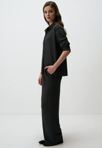 Ensemble deux pièces en tissu côtelé gris foncé ; comprend une chemise à boutons avec des manches retroussées et un pantalon ajusté. Design texturé et minimaliste.