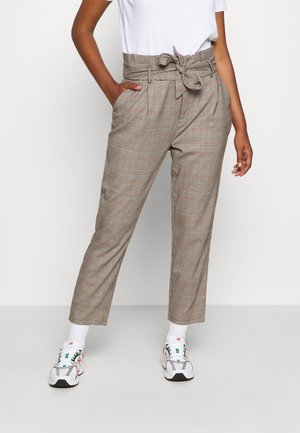 Bruine geruite hoge taille broek met een strikceintuur, voorzien van zijzakken en een taps toelopende pasvorm, gecombineerd met witte sneakers en gestreepte sokken.