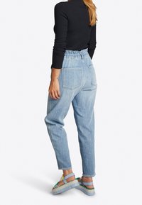 Hochtaillierte hellblaue Denim-Jeans mit lockerer Passform, elastischem Bund und zwei Gesäßtaschen, kombiniert mit mehrfarbigen Plateausandalen.