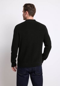 Pull en maille noir avec texture côtelée, col rond et manches longues. Porté sur un jean en denim foncé, mettant en valeur une coupe ajustée.