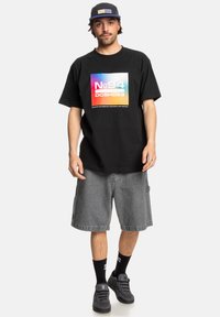 Zwarte t-shirt met korte mouwen met een kleurrijke grafische print, gecombineerd met grijze cargoshorts tot de knie en zwarte sneakers.