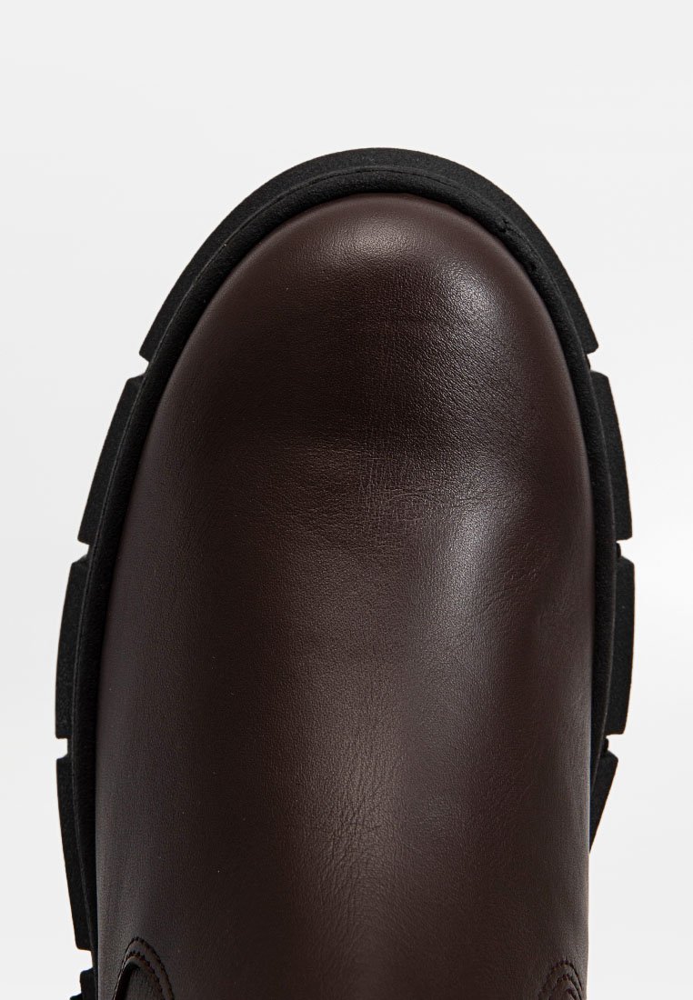 Bottines en cuir marron avec un bout arrondi, une surface texturée et une semelle en caoutchouc noir. Présente des détails de couture le long des bords.