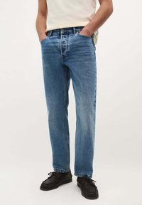 Jeans de mezclilla azul claro con un diseño de pierna recta, cinco bolsillos y cierre de botón. Llevados con zapatos casuales negros.