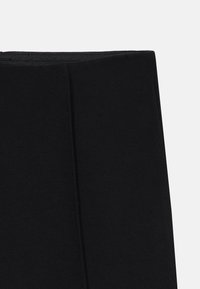 Leggings noirs en tissu extensible, dotés d'une taille haute et d'une texture lisse. Pas de motifs ni d'embellissements visibles.