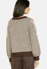 Maglione a righe con orlo a coste marrone. Presenta dettagli floreali rosa sulle spalle. Tessuto morbido e vestibilità rilassata.
