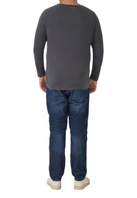 Szara koszula z długim rękawem z raglanowymi rękawami, w połączeniu z niebieskimi dżinsami i białymi sneakersami, widziana od tyłu.