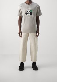 Szara koszulka z krótkim rękawem, z czarno-białą grafiką pandy i zielonym bambusem. Białe szerokie spodnie i czarne botki.