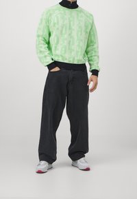 Felpa verde a fantasia con colletto nero, abbinata a jeans scuri oversize e sneaker grigie con dettagli rosa.