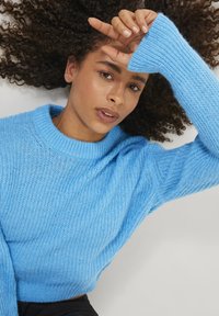 Svetlo modri pleteni pulover z rebrastim okroglim izrezom in dolgimi rokavi, s prostornim krojem in teksturirano tkanino.