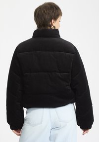 Mustat corduroy-puffatakki, jossa on korkea kaulus, ribbitetty pinta ja ylisuurikokoinen siluetti. Sisältää joustavat hihansuut ja ommellut yksityiskohdat.