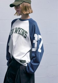 Cămașă cu mânecă lungă, cu blocuri de culoare, având panouri albe și bleumarin, cu litere verzi și numărul "37". Material din bumbac, croi lejer.