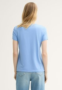 Camiseta de manga corta azul claro en una tela suave, con cuello redondo, que presenta un corte holgado y se combina con jeans de denim claros.