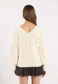 Cream ribbed sweater with a V-back design, featuring long balloon sleeves and a fitted hem, paired with a dark denim mini skirt.