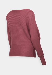 Pull bordeaux côtelé avec un design asymétrique, manches longues et finition texturée. Une fente latérale subtile ajoute un attrait visuel.