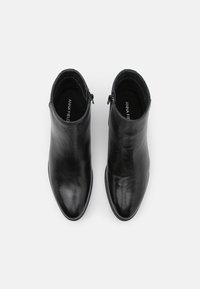 Botines negros de cuero liso con punta afilada, cremalleras laterales y un diseño minimalista. Suelas planas con un sutil brillo.