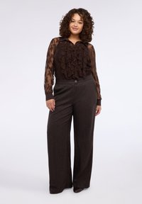 Brązowa przezroczysta bluzka z falbanką z przodu, zestawiona z wysokim stanem i szerokimi nogawkami spodni ozdobionych subtelnymi akcentami z metalicznej nici.