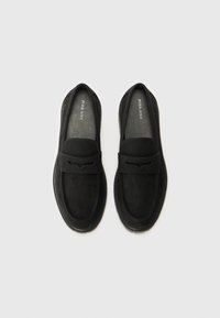 Schwarze Wildleder-Loafer mit glatter Textur, ausgestattet mit einem breiten Riemen über dem Fußrücken und einem dezenten Ausschnitt-Design. Flache Sohle, zum Hineinschlüpfen.