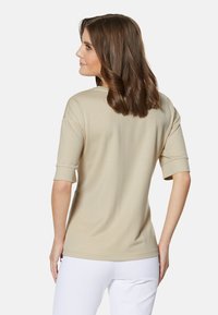 Beige T-shirt met korte mouwen, een ronde hals, een zachte textuur en een ontspannen pasvorm, gecombineerd met witte broeken, gezien vanuit de achterkant.
