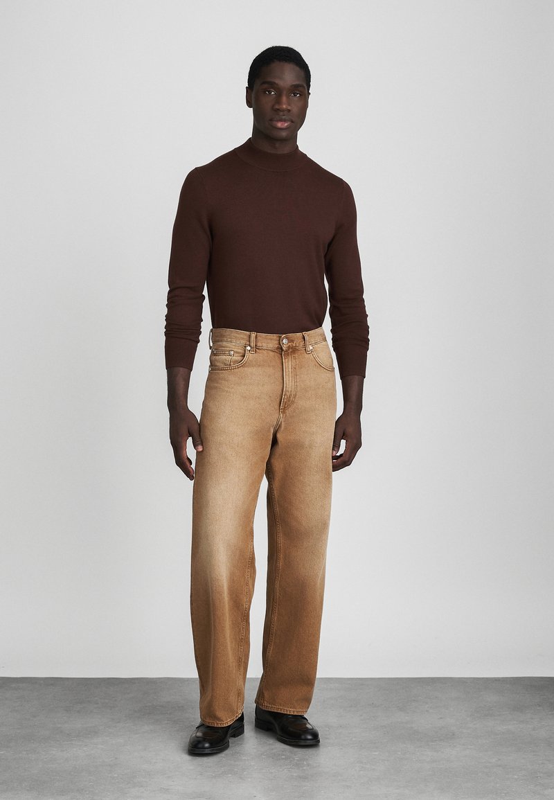 Brun turtle neck sweater parret med lysebrune brede bukser. Bukserne har subtil blegning, frontlommer og en klassisk lynlås.