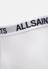 Vita boxershorts med en jämn textur, med ett brett elastiskt midjeband märkt "ALLSAINTS" i svarta bokstäver.