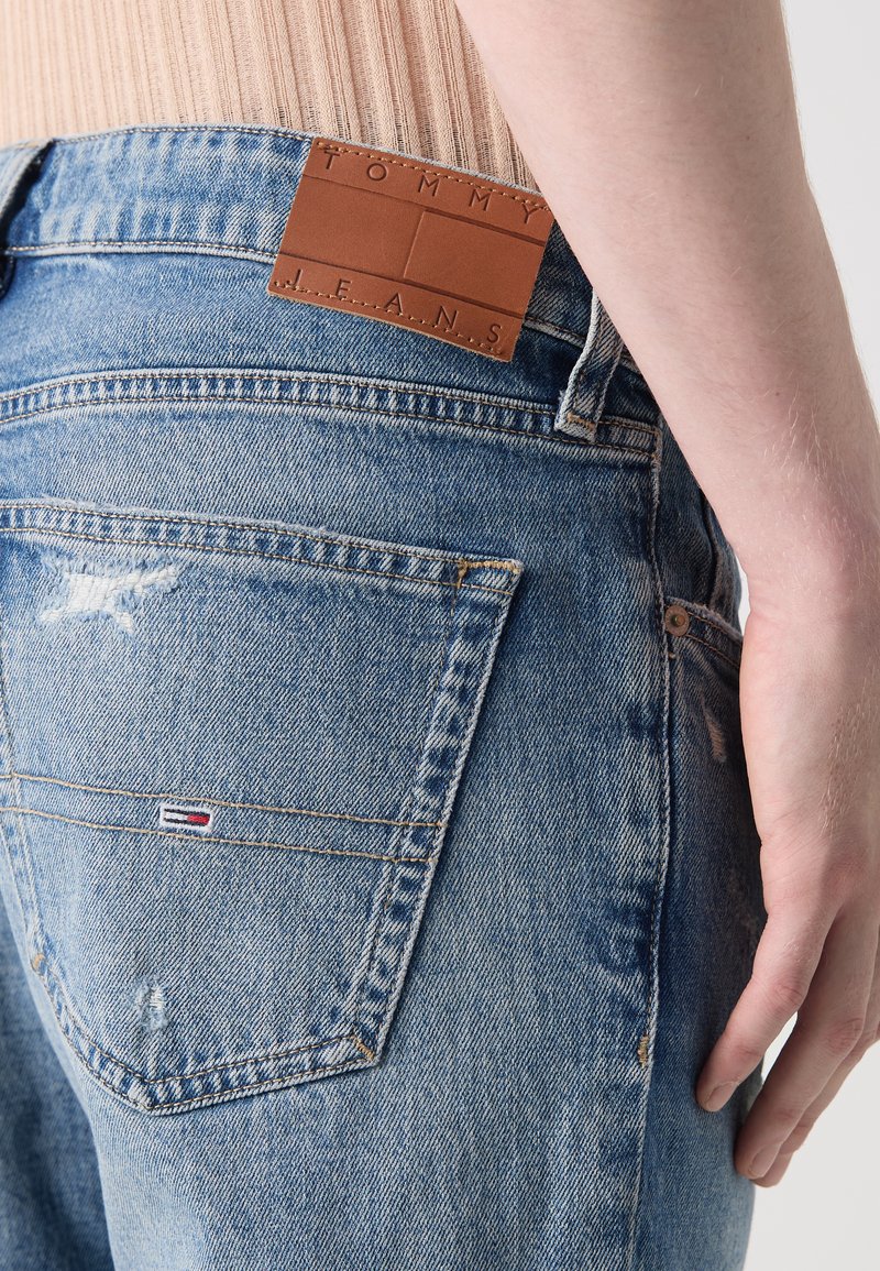 Blaue Jeans aus Denim mit heller Waschung, mit einem braunen Lederpatch auf der Rückseite, das "TOMMY JEANS" eingestanzt hat, sowie einem kleinen Logo in der Nähe der Tasche.