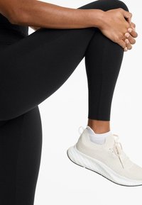 Mustat leggingsit sileällä pinnalla, yhdistettynä valkoisiin neulossneakereihin, joissa on teksturoitu päällinen ja paksu, pehmeä pohja.
