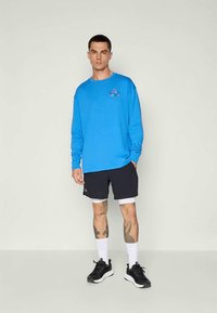 Mėlyna ilgaa rankovė marškiniai su logo, derinami su juodais šortais ir baltais legginsais po jais. Juodi sportbačiai ir balti kojinės užbaigia aprangą.