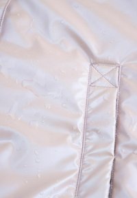 Jasno beżowa wodoodporna tkanina z kroplami wody oraz wzmocnioną, przeszywaną prostokątną łatą.