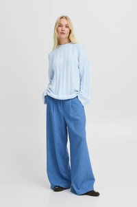 Hellblauer Strickpullover mit geripptem Muster, weiten Ärmeln, kombiniert mit lässigen, weit geschnittenen hellblauen Hosen, die eine entspannte Silhouette schaffen.