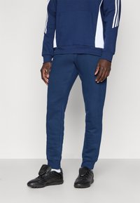Navy sweatshirt with white side accents and ribbed cuffs paired with matching navy sweatpants. Black athletic shoes complete the outfit.