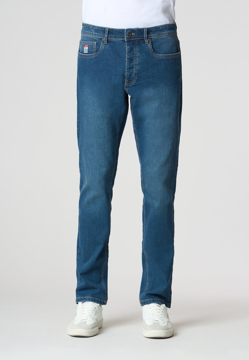 Jeans in denim blu con una vestibilità dritta, dotati di cinque tasche, una leggera scoloritura e una patch del marchio sulla tasca posteriore. Indossati con sneakers bianche.