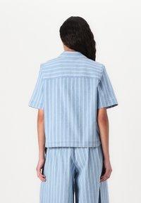 Camicia azzurra a maniche corte in tessuto denim con strisce verticali bianche, colletto standard e vestibilità rilassata e corta.