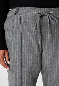Grijze gestreepte joggingbroek met een trekkoord in de taille, zijzakken en een zachte textuur, voorzien van witte verticale strepen en accenten in zilverkleurig metaal.