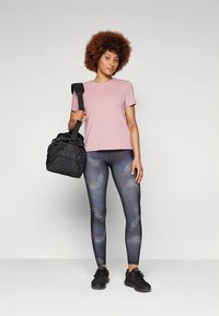 T-shirt en coton rose pâle associé à des leggings bleu marine avec un motif texturé, sac de sport noir et baskets noires. Design et coupe simples.