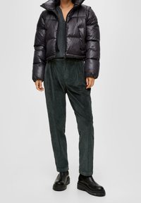 Doudoune noire à la coupe courte, associée à un pantalon en velours côtelé vert foncé. Des bottes chunky noires à la cheville complètent la tenue.