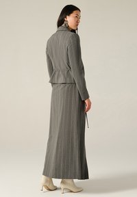 Completo grigio a righe con dettaglio peplum, gonna lunga e maniche lunghe. Tessuto dalla superficie liscia, abbinato a stivali con tacco di colore crema.