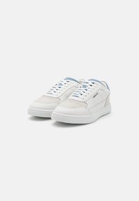 Zapatillas de cuero blanco con acentos en azul claro, detalles perforados, cordones planos y una suela de goma blanca texturizada. Diseño de punta redondeada.