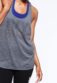 Canottiera grigia sportiva con colletto blu, caratterizzata da un design in rete e dettagli testuali. Abbinata a leggings neri con tasche laterali discrete.