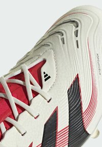 Weiße und rote Fußballschuhe aus strukturiertem synthetischem Material, mit schwarzen Akzenten, schrägen Streifen und einem markanten Schnürdesign.