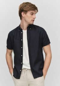 Kortärmad marinblå skjorta med knappar, tillverkad av lätt tyg, kombinerad med en vit T-shirt och ljusbeiga byxor. Slät textur, avslappnad passform.