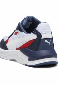PUMA tennisjalatsid, millel on tume sinine ja valge pealis, punaste aktsentidega. Tekstuuritud pinnad ja logo detail kanna peal. Kaasaegne, sportlik disain.