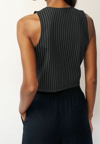 Top nero senza maniche con righe bianche verticali, caratterizzato da un design aderente e una texture a costine, abbinato a pantaloni scuri.