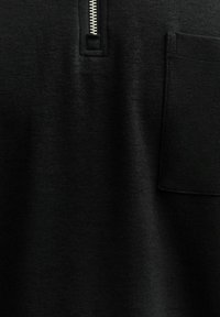 Zwarte sweatshirt met een kwart-rits kraag, voorzien van een kleine borstzak. Het materiaal lijkt zacht met een gladde textuur.
