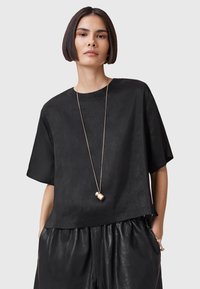 Svart kortärmad topp i texturerat tyg, med en avslappnad passform och rundad halsringning. Bärs med ett långt, metalliskt hänge på halsband.