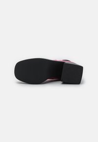 Suela de zapato de tacón alto con una base de goma negra, que presenta una textura suave y un ligero tacón, complementando una parte superior rosa.