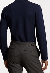 Marinblå stickad tröja med krage, i kombination med grå ullbyxor med detaljer som knapp och tab, som betonar en skräddarsydd passform.