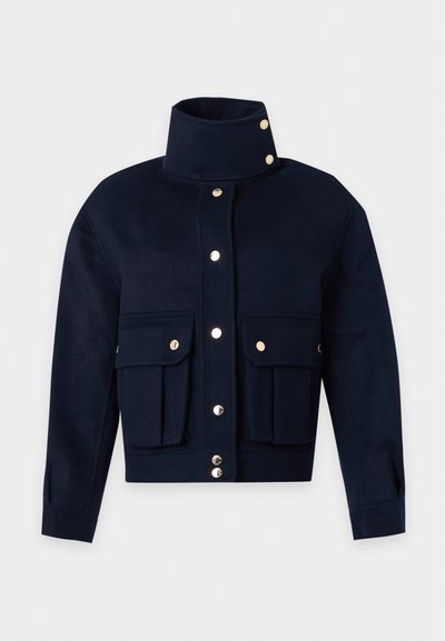 Veste bleu marine foncé avec col montant, boutons-pression dorés sur le devant et deux grandes poches à rabat sur la poitrine.