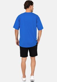 T-shirt en coton bleu royal avec des manches courtes, un col rond et une coupe décontractée. Associé à un short noir et des baskets blanches.