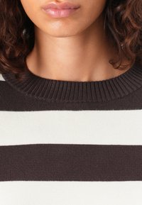 Csíkos pulóver széles krémszínű és barna vízszintes csíkokkal, kerek nyakkivágással és bordázott textúrával a nyakrészen.